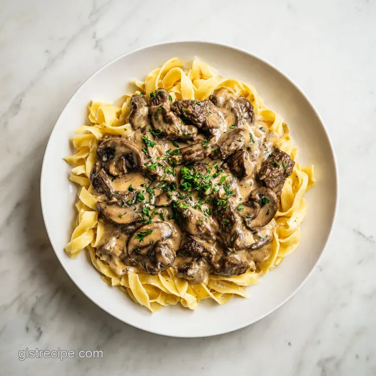 Beef stroganoff artfully swirled in a white bowl, garnished with chives. Velvety smooth.