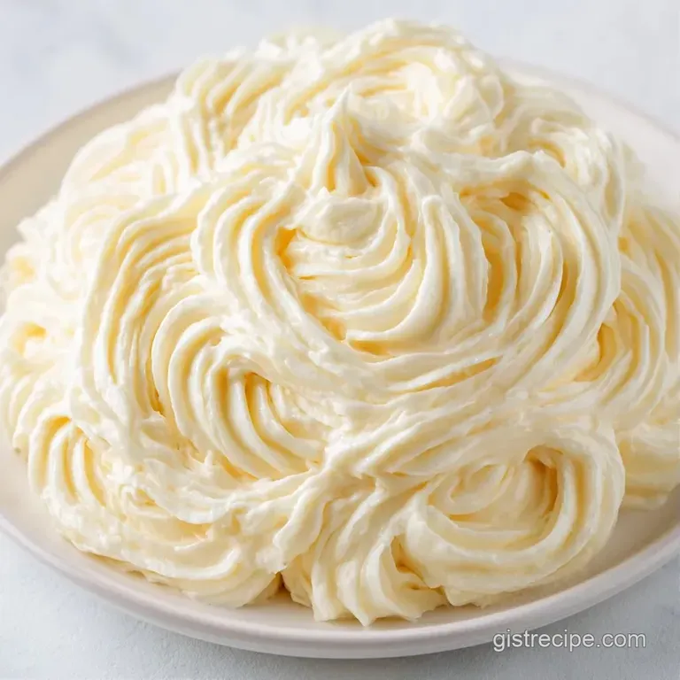 Swirls of snow-white whipped frosting piped high on a cake slice with a small gold spoon resting nearby.