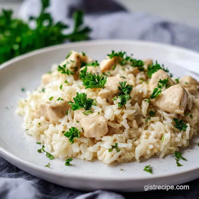 A neat mound of creamy chicken and rice on a ceramic plate, garnished with fresh green parsley and cracked pepper.