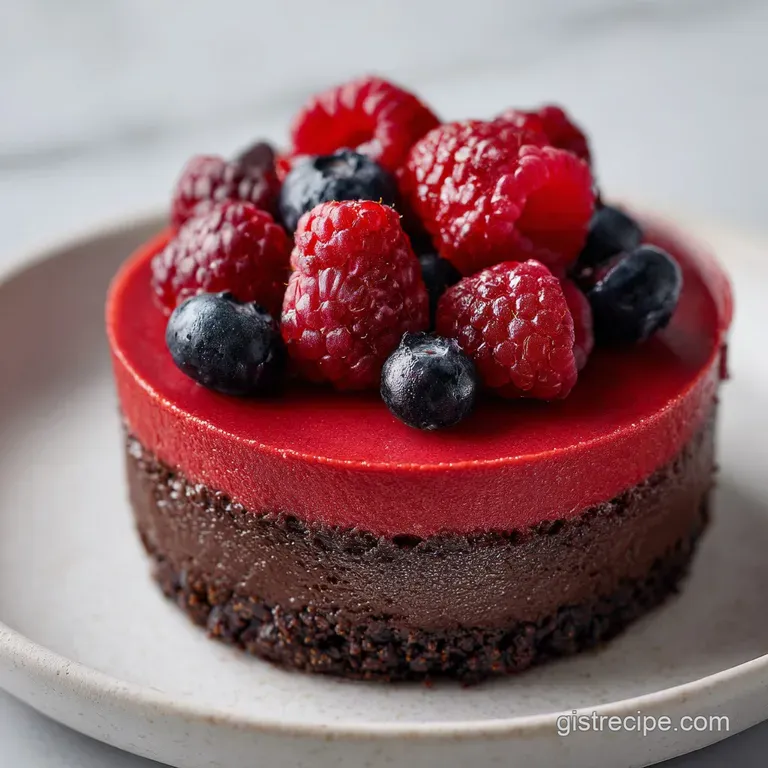 A neat slice of dark chocolate cake on a white plate, drizzled with bright red raspberry coulis and fresh mint.