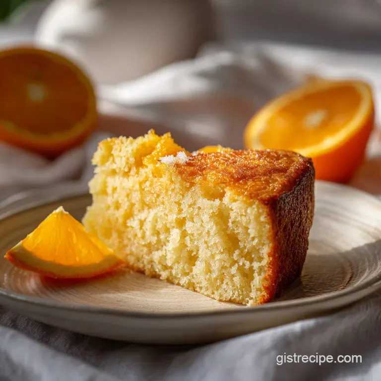 A slice of moist orange cake, showing its tender crumb, on a white plate with fresh orange zest.