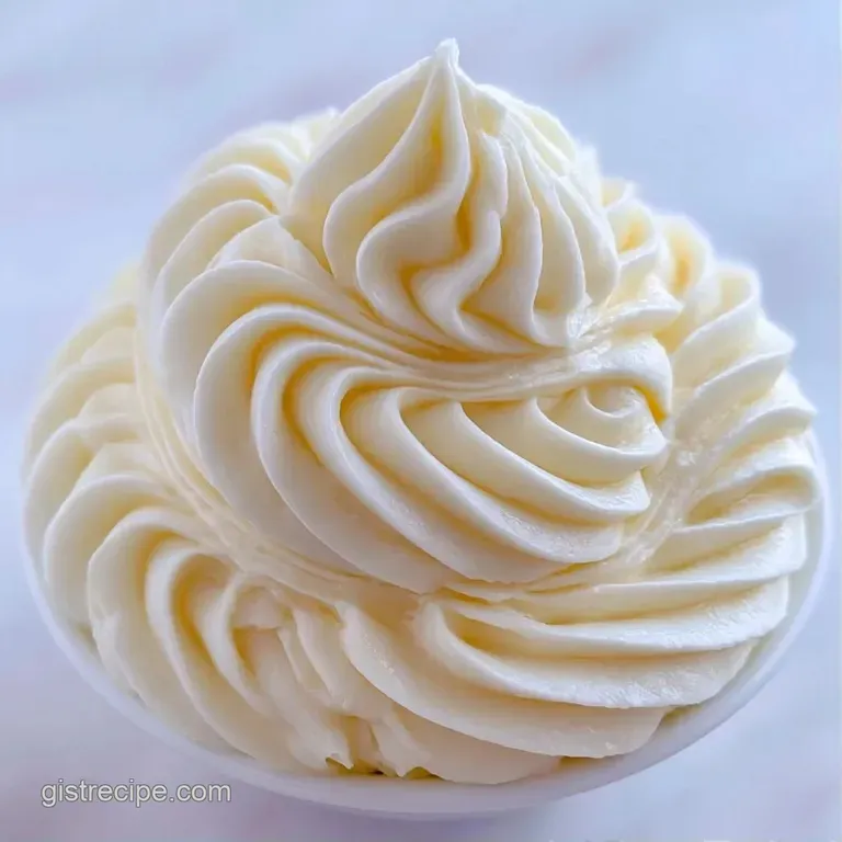 Fluffy swirls of thick white icing topping golden cupcakes arranged on a tiered white marble dessert platter.