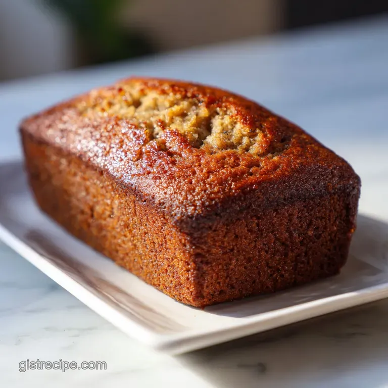 Slices of moist banana bread with a dusting of powdered sugar, alongside fresh banana slices on a clean white plate. Comfo...