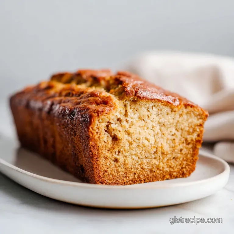 A rustic slice of banana bread, dusted with powdered sugar, sits on a wooden board with a fork.
