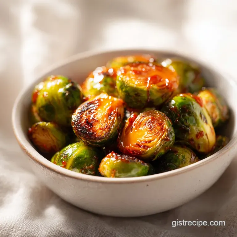 Roasted green sprouts glazed in a sticky reddish-orange sauce, garnished with sesame seeds on a modern slate plate.
