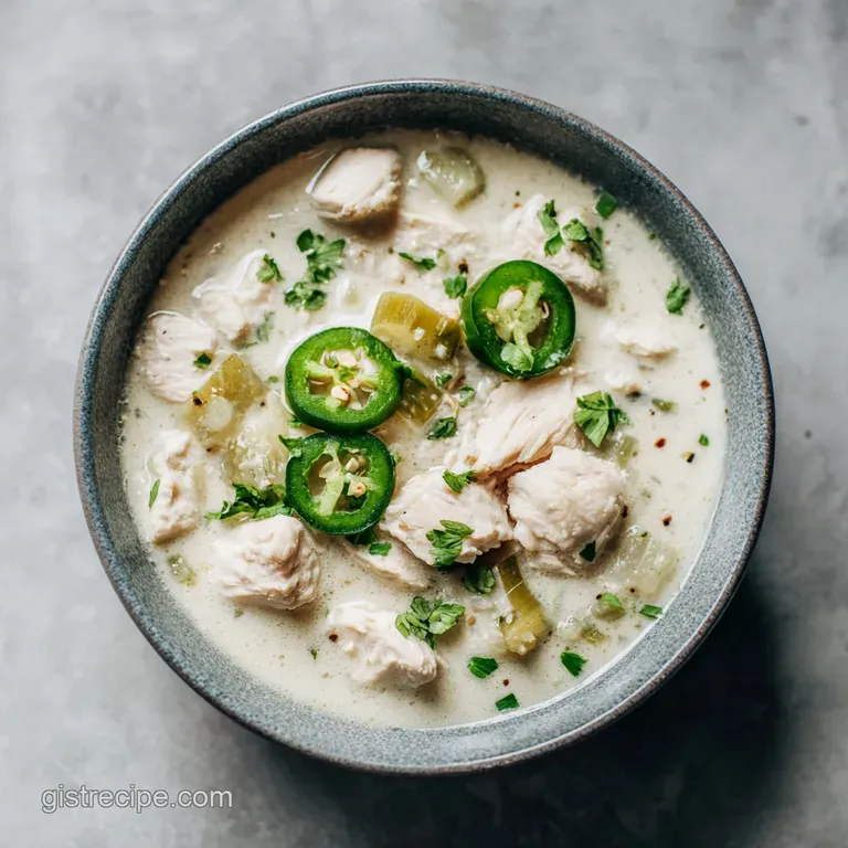 Elegant bowl of white chicken chili, garnished with cilantro and lime. Steam rises from the creamy, comforting dish.