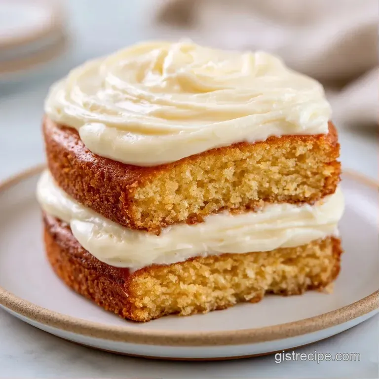 A tall slice of golden sponge cake with thick white frosting and a fresh strawberry on a minimalist ceramic plate.