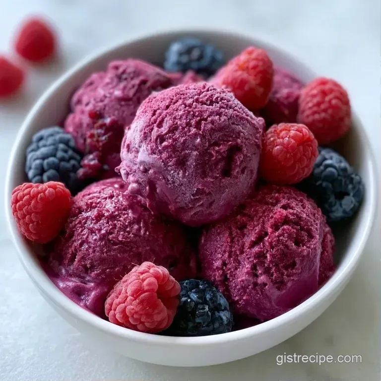 Three elegant scoops of deep purple frozen dessert topped with fresh berries and a sprig of mint in a glass bowl.