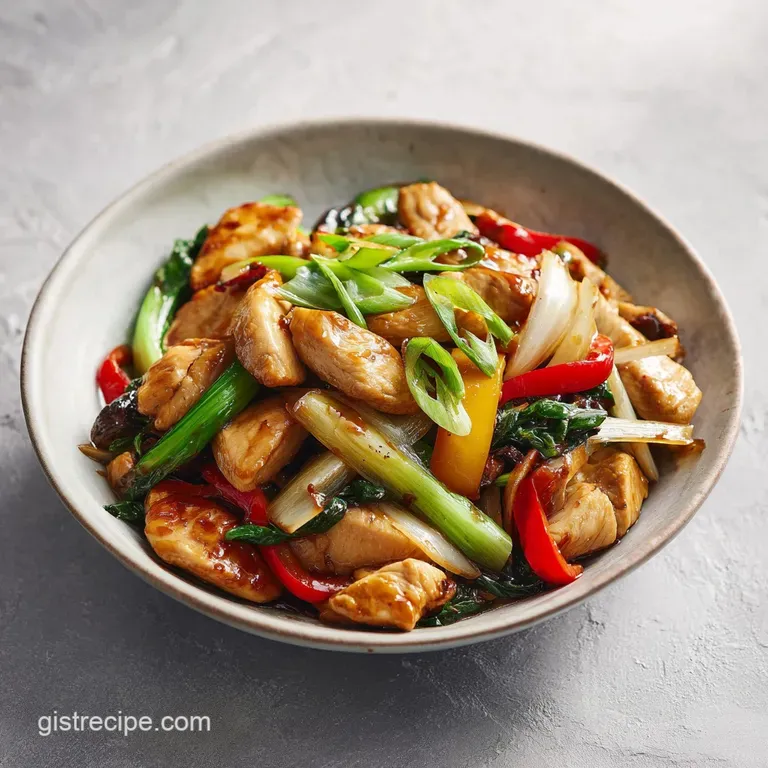 Chicken stir-fry artfully arranged on a white plate with vibrant green scallions sprinkled on top. Sauce shimmers under br...