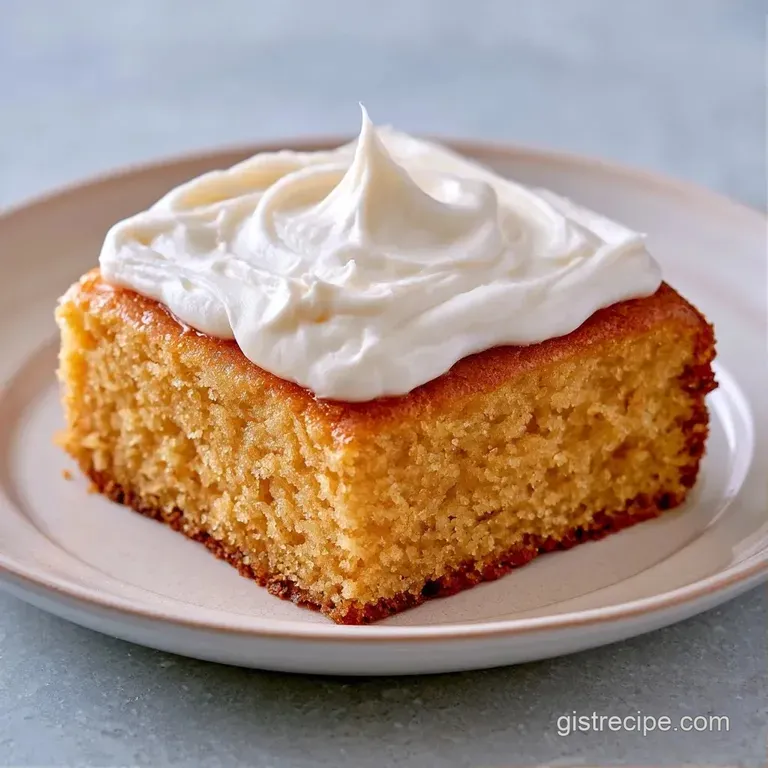 A neat square slice of pale gold cake with thick white icing, served on a white ceramic plate with a silver fork.