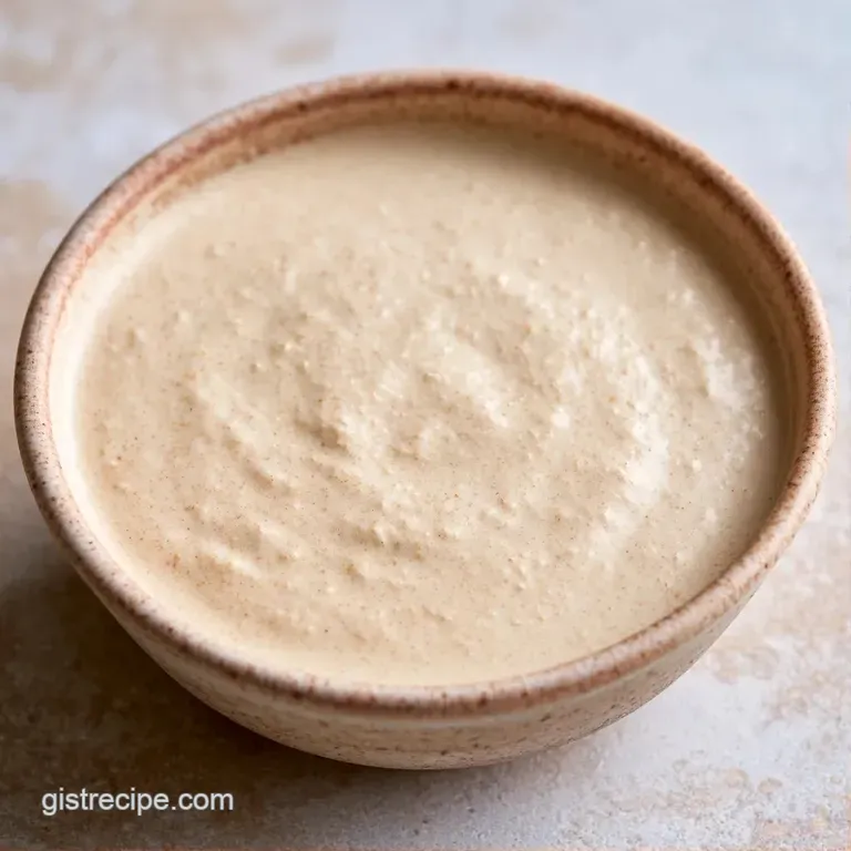 A small white ceramic bowl of velvety beige sauce paired with a fresh garden salad on a light linen tablecloth.