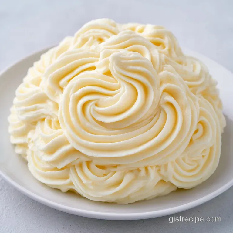 A swirl of pale ivory frosting on a white ceramic plate, garnished with a delicate, bright green mint leaf.